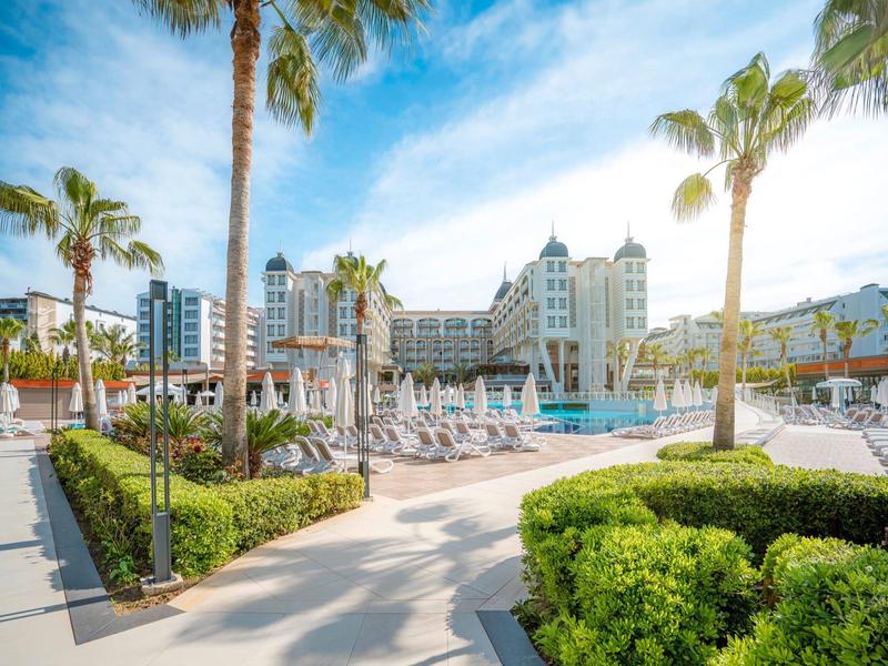 Luxury hotel with pool, lounge chairs, and palm trees under a clear blue sky.
