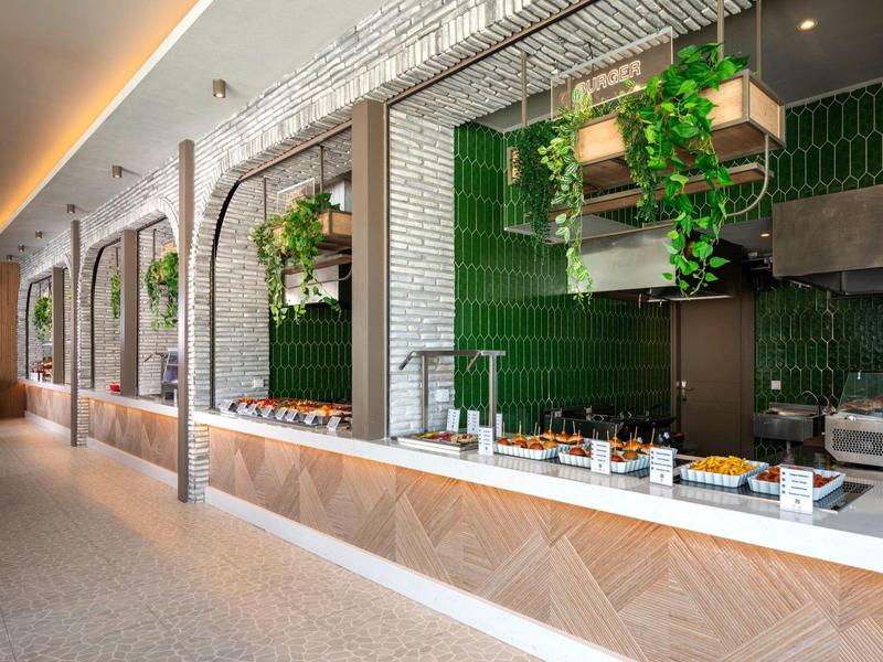 Modern buffet area with green wall tiles and plants in a hotel.