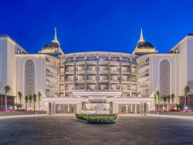Wide view of a luxury hotel at night with illuminated entrance and colorful sky.