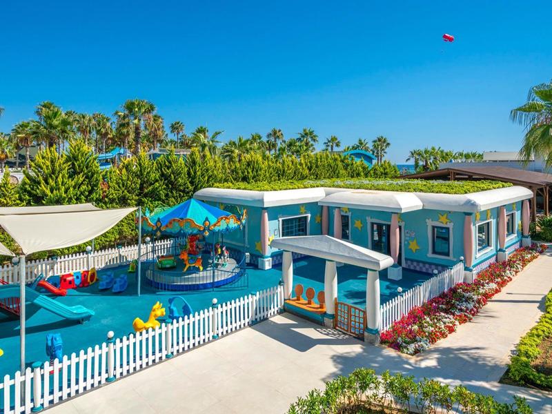 Colorful kid-friendly accommodation with playground, fences, and flowers under blue sky.