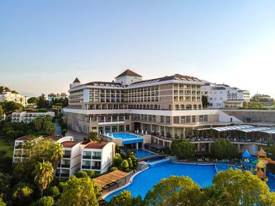 Großes Hotel mit mehreren Stockwerken, umgeben von Palmen und einem blauen Pool bei klarem Himmel.