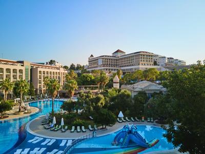 Luxury hotel with large pool, surrounding sun loungers, and lush greenery under clear sky.