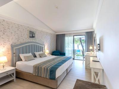 Bright hotel room with double bed, nightstands, flat-screen TV, and access to a balcony with nature view.