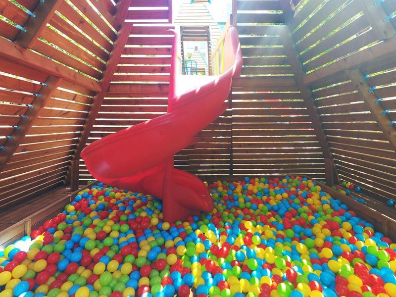 Kolorowy basen z kulkami z czerwoną zjeżdżalnią w drewnianym wnętrzu
