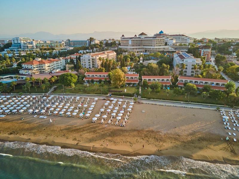 Widok na plażę z leżakami i hotelami w tle pod czystym niebem.