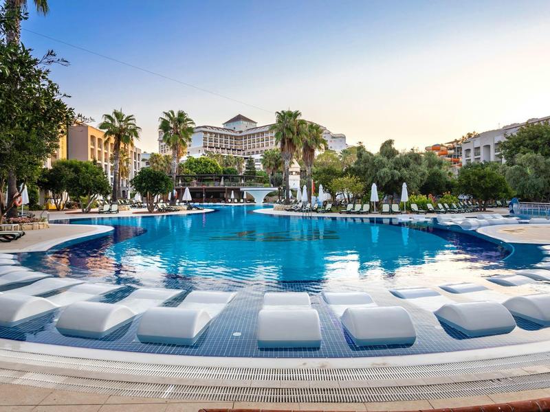 Duży basen hotelowy z palmami i leżakami o zachodzie słońca.