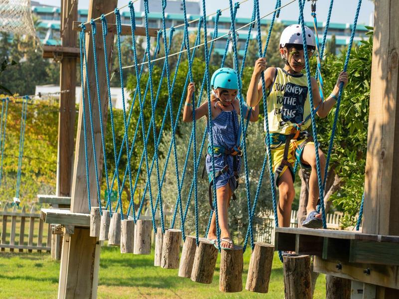 Dzieci balansujące na zewnętrznym torze przeszkód na linach i drewnianych deskach.