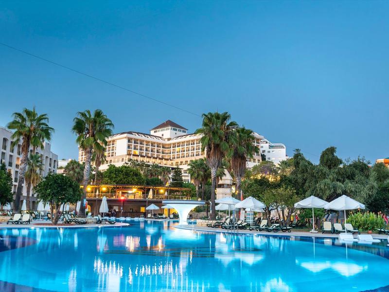 Luksusowy hotel z dużym basenem, palmami i leżakami pod czystym niebem.