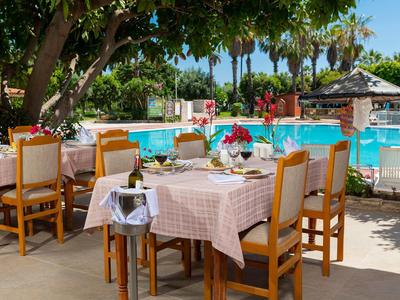 Freiluftrestaurant mit gedeckten Tischen, Holzmöbeln und Swimmingpool umgeben von Palmen.