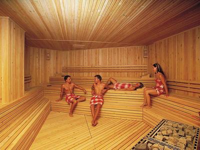 Saunaraum aus hellem Holz mit vier Personen, die in rot gemusterten Handtüchern entspannen.