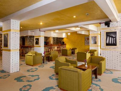 Gemütlicher Raum mit grünen Sesseln, Bar, dekorativen Säulen und warmen gelben Wänden.