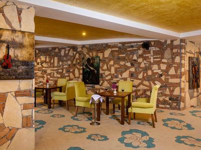 Gemütlicher Raum mit gelben Sesseln, Holztischen und Steinwänden, Teppich mit blauem Muster.