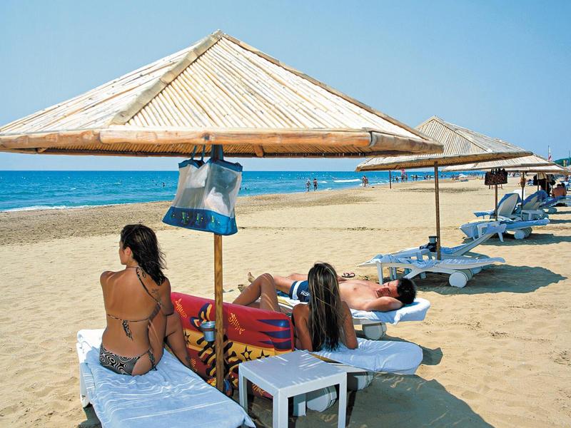 Strand mit Sand, Liegestühlen, Strohdächern und Menschen, die sich in der Sonne entspannen.