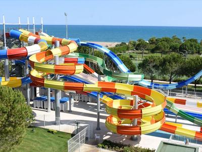 Parco di scivoli d'acqua colorati vicino al mare con aree verdi e alberi in primo piano.
