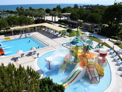 Gran piscina al aire libre con toboganes y zona infantil junto a tumbonas y jardín cerca del mar.