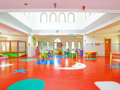 Gran sala multifuncional luminosa con suelo rojo y sillas de colores en una guardería.