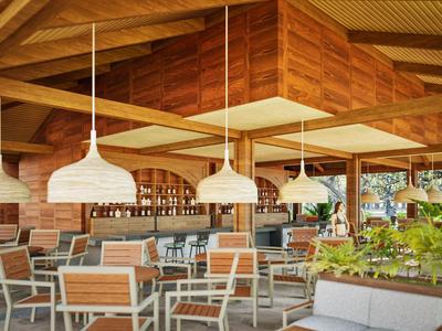 Restaurante moderno de hotel con lámparas y sillas de madera, rodeado de ventanas de vidrio y plantas.