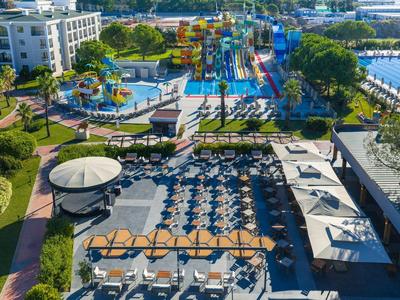 Vista aérea del área de piscina de un hotel con tumbonas, sombrillas y parque acuático al fondo.