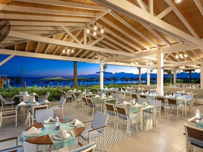 Restaurante al aire libre con mesas preparadas y vista al mar al anochecer.