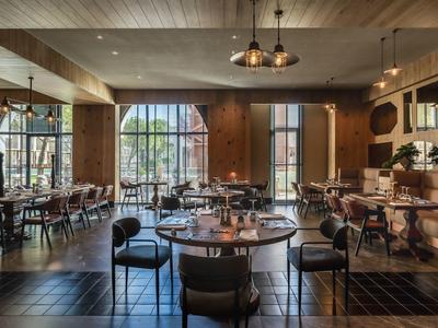 Restaurante elegante con mesas de madera, sillas y grandes ventanas que dejan entrar la luz del día.