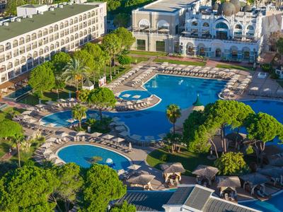 Duży basen hotelowy z leżakami i obfitością zieleni w słonecznym otoczeniu.