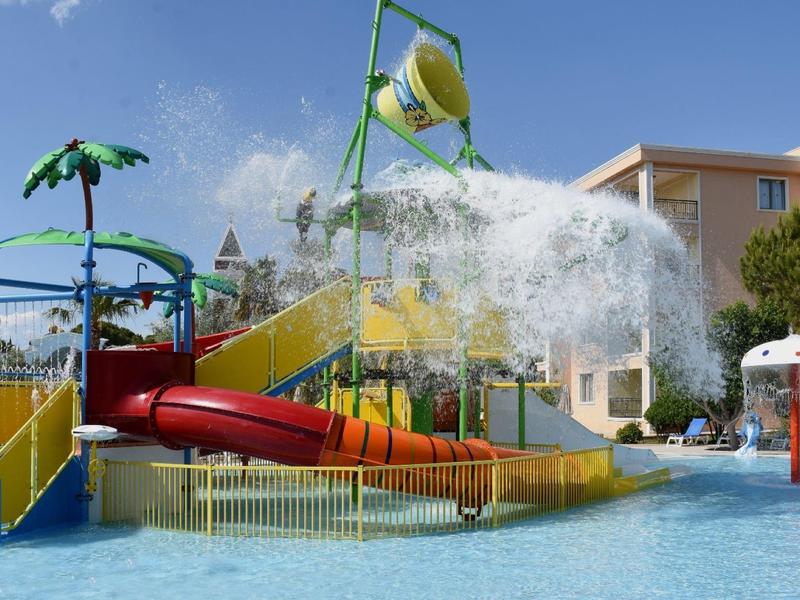 Parque acuático en la piscina del hotel con tobogán, palmeras y fuentes de agua bajo cielo azul.