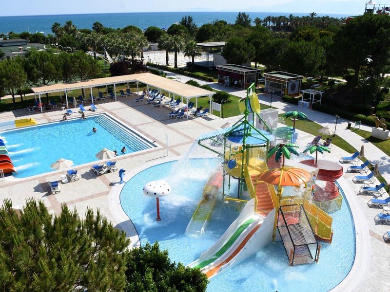 Gran piscina al aire libre con toboganes y zona infantil junto a tumbonas y jardín cerca del mar.