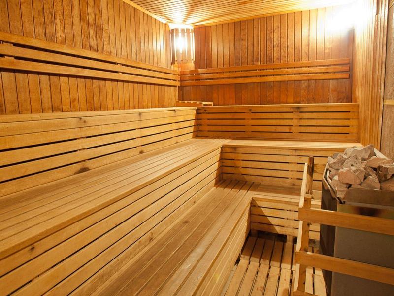 Sauna de madera clara con bancos escalonados y estufa con piedras.