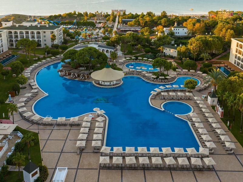Gran piscina de hotel con forma inusual, rodeada de tumbonas y edificios.