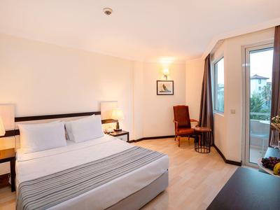 Helles Schlafzimmer mit Doppelbett, Nachttischen, Stuhl, Tisch, Balkon und Obstschale auf Kommode.