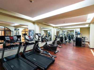 Heller Fitnessraum mit Laufbändern, Crosstrainern, Spiegeln und Holzboden.