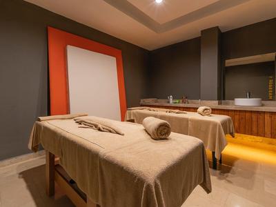 Gemütlicher Wellnessraum mit zwei Massageliegen, warmen Braun- und Orangetönen und sanfter Beleuchtung.