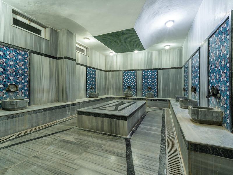 Interiores de un baño turco con azulejos azules y bancos de mármol gris claro.