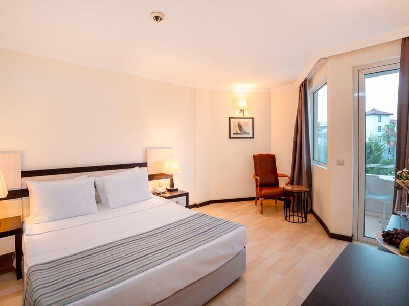 Habitación de hotel acogedora con cama doble, lámparas de noche y balcón con vista al jardín.