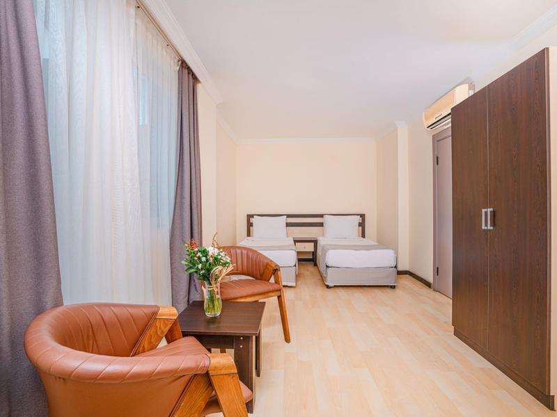 Habitación de hotel luminosa con dos camas, sillones de cuero, armario y ventana con cortinas.