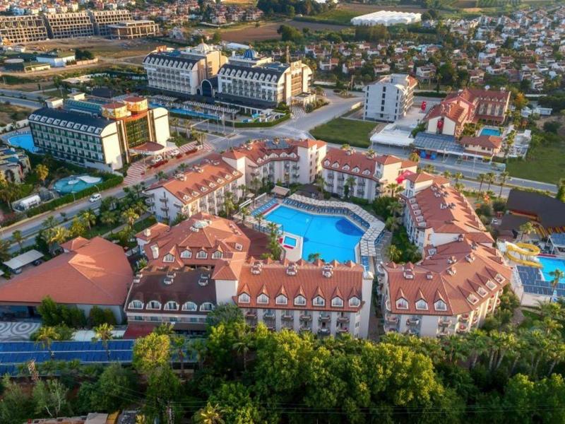 Gran complejo hotelero con varios edificios y piscinas, rodeado de áreas verdes y vista a la ciudad.