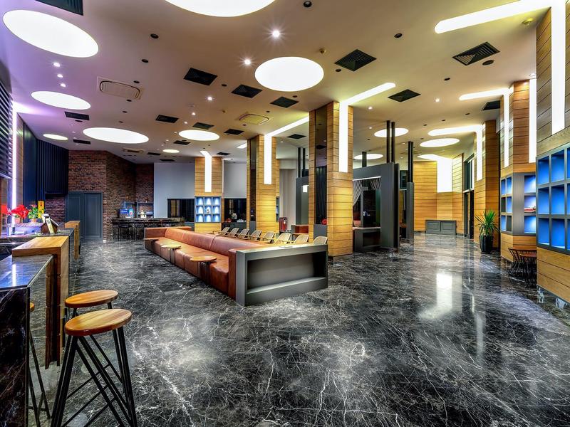 Área de lounge moderna de hotel con suelo de mármol brillante, bancos y iluminación indirecta.