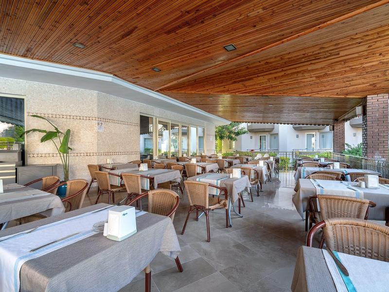 Área exterior cubierta de un restaurante con mesas preparadas y techo de vigas de madera.