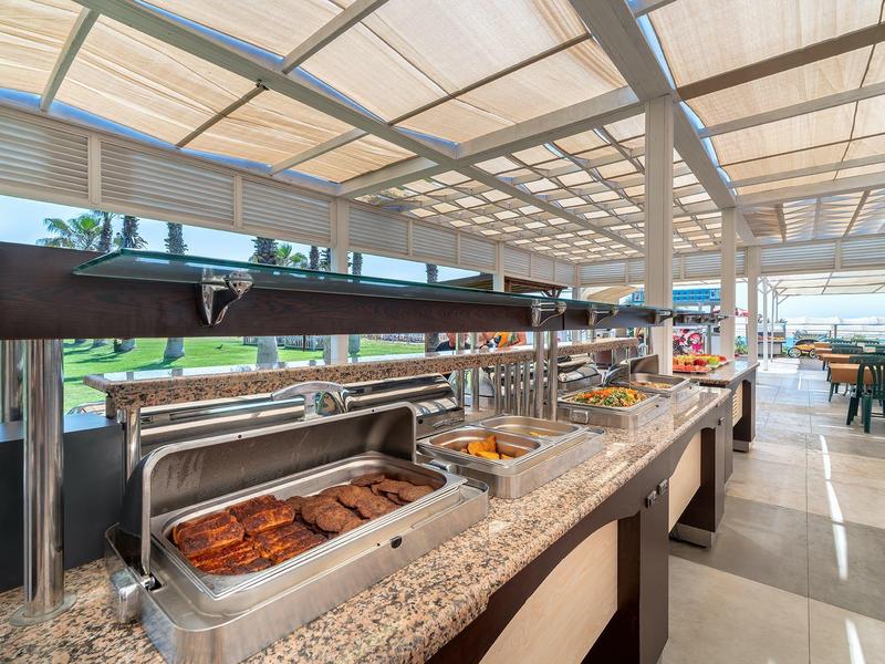 Buffet con varios platos calientes en un área exterior cubierta y luminosa de un hotel.