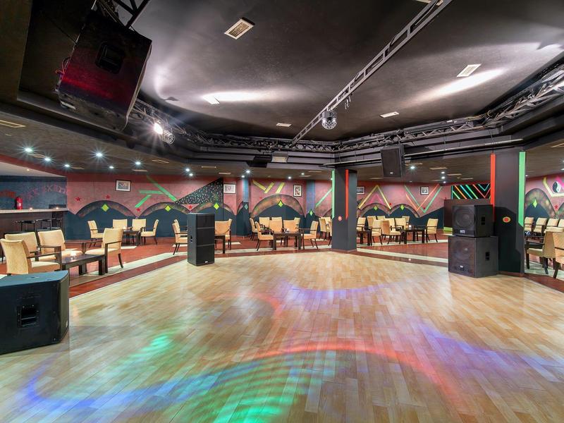 Gran sala de eventos con pista de baile, equipos de sonido y áreas de descanso cómodas en las paredes.