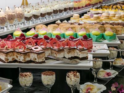 Mehrstöckige Auswahl bunter, kunstvoll dekorierter Desserts und Törtchen auf Glasplatten.