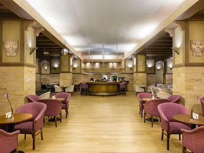 Großer Hotel-Lobby mit Holzboden, violetten Sesseln, Tischen und zentralem Empfangstresen.