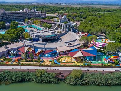 Großer Freizeitpark mit bunten Wasserrutschen, Pools, grünen Bäumen und einem Fluss vorne.