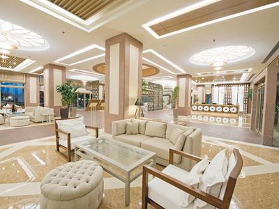 Hall d'hôtel lumineux avec coins salons modernes, luminaires décoratifs au plafond et sol poli.