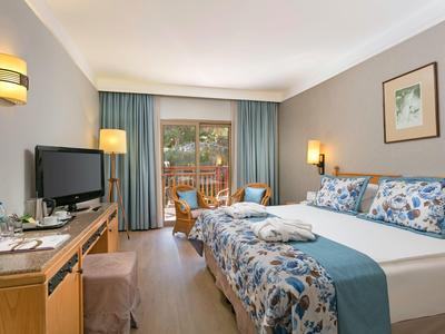 Gemütliches Hotelzimmer mit Doppelbett, Flachbildschirm, Balkon und Holzmöbeln in warmen Farben.