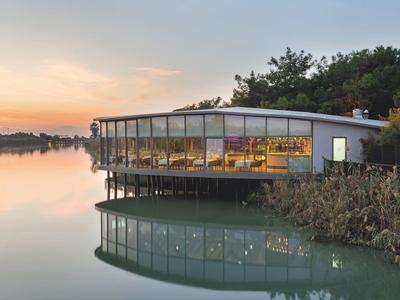 Hôtel moderne avec grande façade vitrée au bord d'un lac calme au coucher du soleil