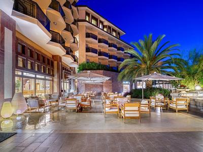 Espace extérieur d'un hôtel avec sièges confortables, palmiers et ambiance détendue en soirée.