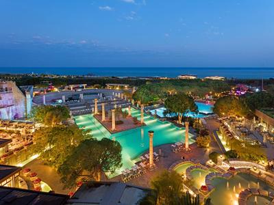 Blick auf eine beleuchtete Hotelanlage mit Pools und Palmen bei Abenddämmerung am Meer.