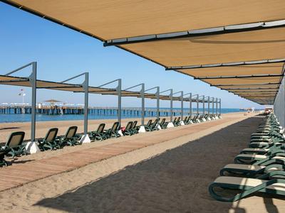 Reihe von grünen Liegen unter großen Sonnensegeln an einem sonnigen Sandstrand am Meer.