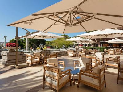 Große Terrasse mit Holzstühlen und Tisch unter weißen Sonnenschirmen, blauer Himmel im Hintergrund.